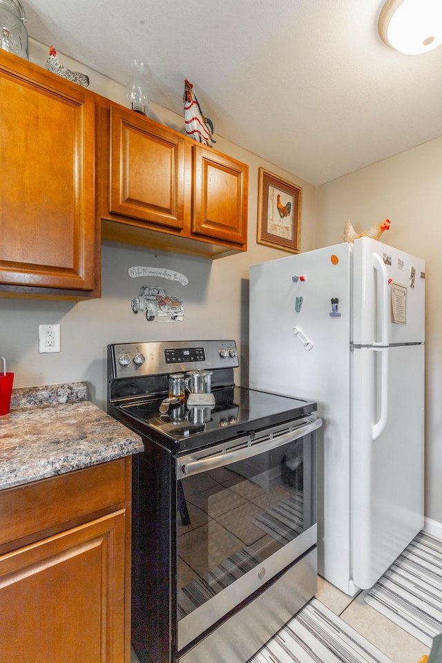 kitchen featuring freestanding refrigerator, brown cabinets, light tile patterned flooring, and stainless steel electric stove