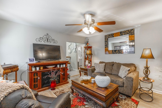 living area featuring ceiling fan, a fireplace, wood finished floors, and baseboards