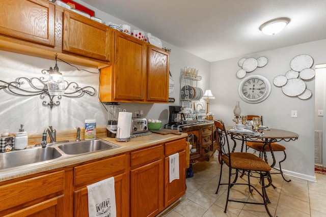 kitchen with brown cabinetry, light tile patterned floors, light countertops, and a sink