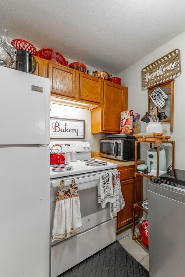 kitchen with white appliances, brown cabinets, a textured ceiling, and light tile patterned flooring