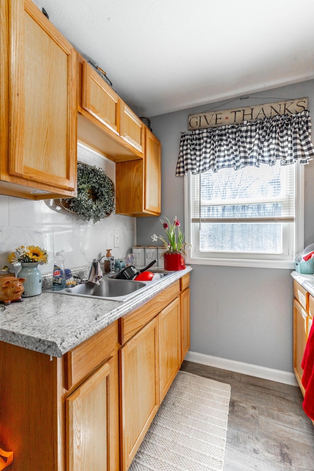 kitchen with a sink, baseboards, light countertops, light wood-type flooring, and backsplash