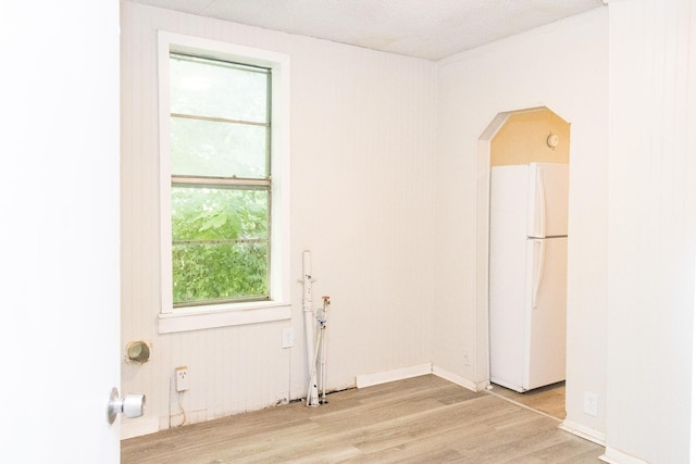 unfurnished room with arched walkways, light wood-style flooring, and baseboards