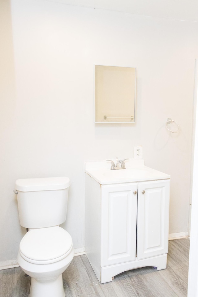 bathroom featuring toilet, baseboards, wood finished floors, and vanity