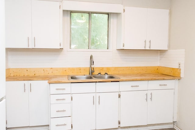 kitchen featuring white cabinets, backsplash, light countertops, and a sink