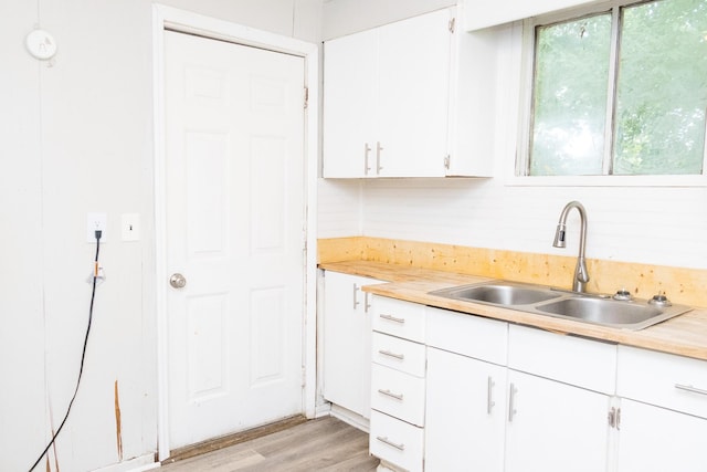 kitchen featuring light wood-type flooring, white cabinets, light countertops, and a sink