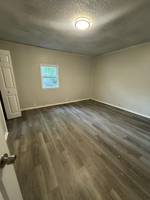 empty room featuring dark wood-type flooring, a textured ceiling, and baseboards