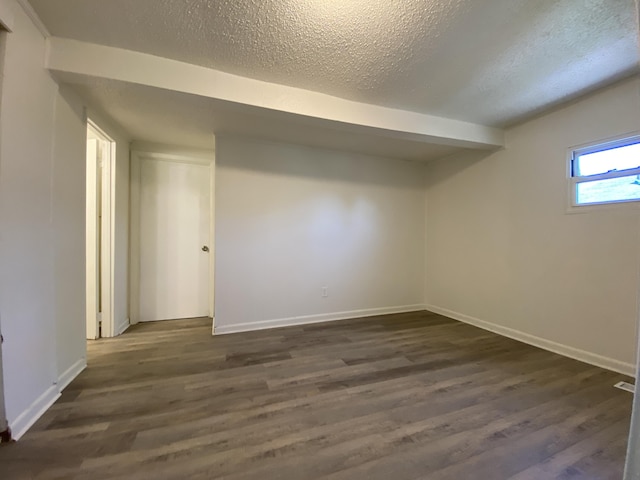 basement with a textured ceiling, dark wood-style flooring, and baseboards