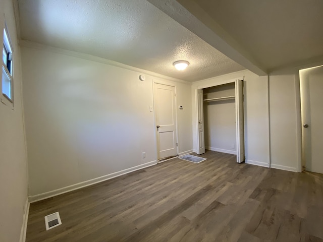 unfurnished bedroom with dark wood-style floors, a closet, visible vents, a textured ceiling, and baseboards