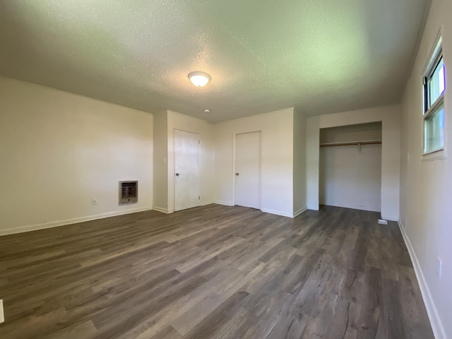 unfurnished bedroom featuring a textured ceiling, baseboards, a closet, heating unit, and dark wood-style floors