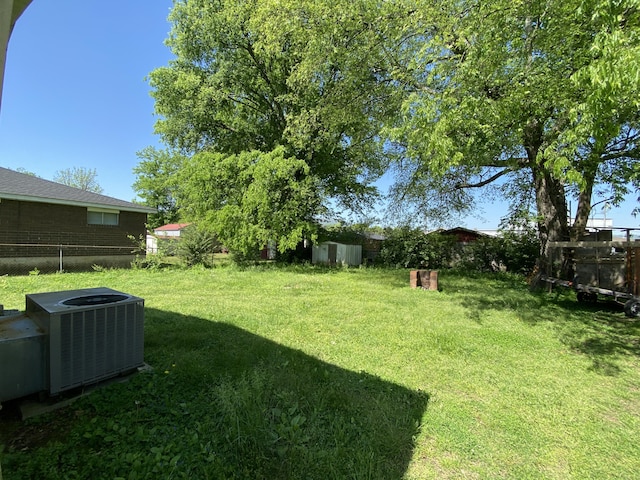 view of yard featuring a storage shed, an outdoor structure, fence, and central air condition unit