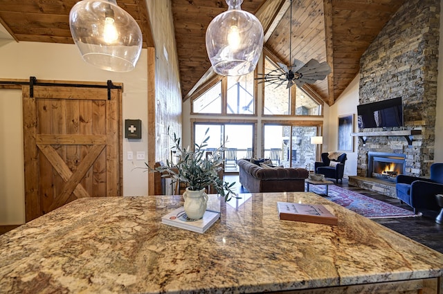 kitchen featuring light stone counters, a barn door, a fireplace, wood ceiling, and a ceiling fan