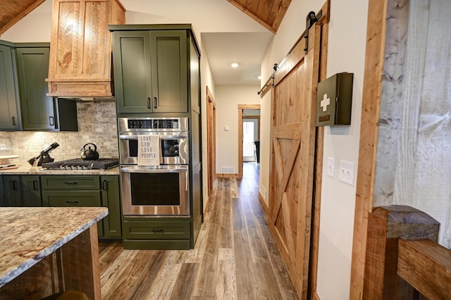 kitchen with green cabinets, stainless steel appliances, a barn door, and decorative backsplash