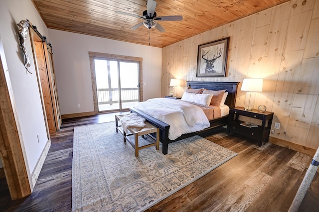 bedroom featuring a barn door, wooden ceiling, wooden walls, wood finished floors, and baseboards