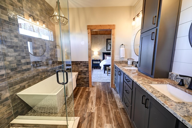 ensuite bathroom featuring double vanity, a sink, ensuite bath, and wood finished floors