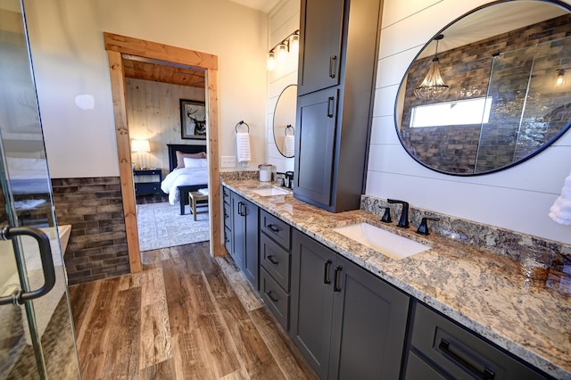 full bath with double vanity, a tile shower, a sink, and wood finished floors