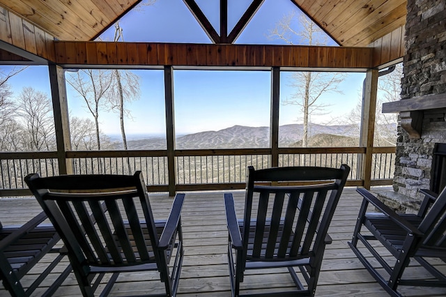 unfurnished sunroom with lofted ceiling, wood ceiling, an outdoor stone fireplace, and a mountain view