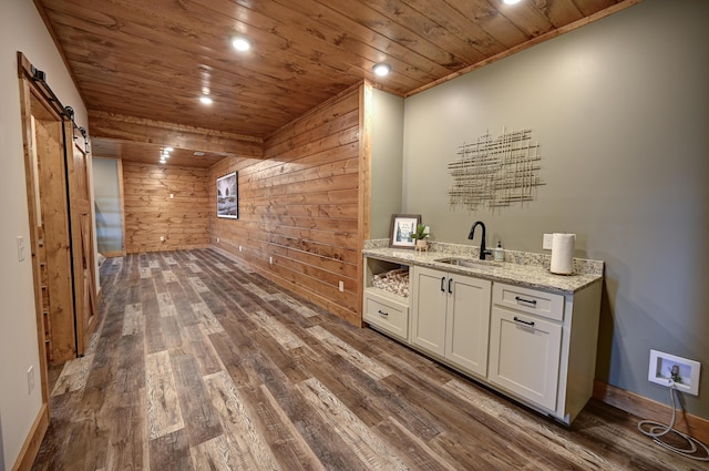 bar featuring a barn door, wooden walls, wood ceiling, dark wood-style flooring, and a sink