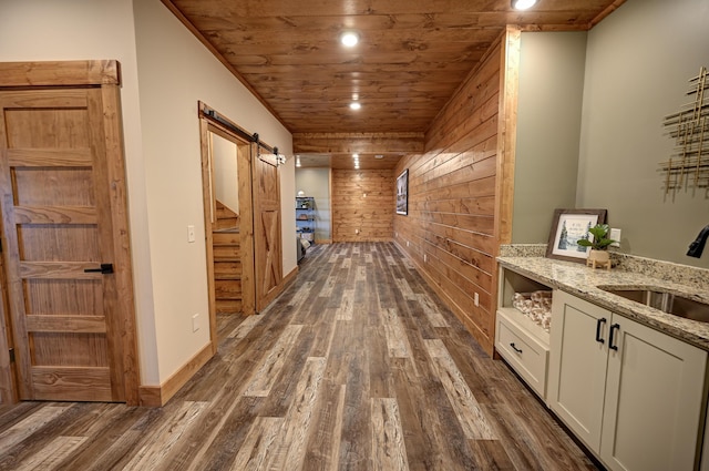 hall featuring a barn door, wood ceiling, dark wood-style flooring, wood walls, and a sink