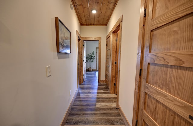 corridor with dark wood-type flooring, wood ceiling, and baseboards