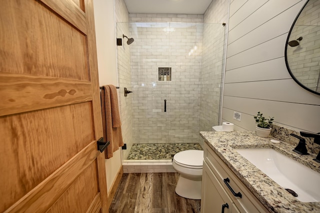 full bath featuring toilet, wooden walls, wood finished floors, vanity, and a stall shower