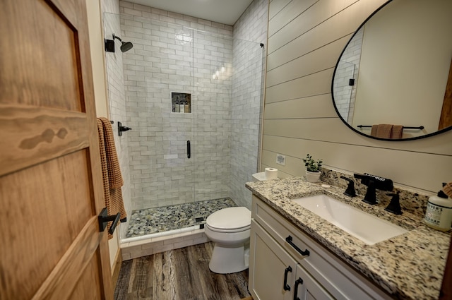 bathroom featuring toilet, wood walls, wood finished floors, vanity, and a shower stall