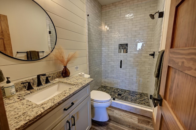 bathroom featuring wooden walls, toilet, wood finished floors, vanity, and a shower stall