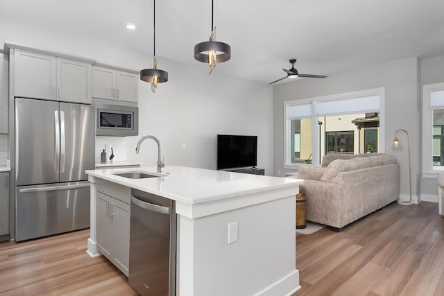 kitchen featuring stainless steel appliances, light countertops, backsplash, open floor plan, and a sink