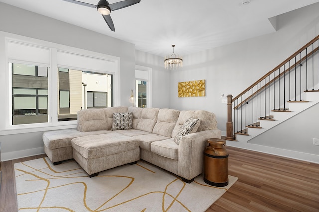 living room with baseboards, stairway, wood finished floors, and ceiling fan with notable chandelier