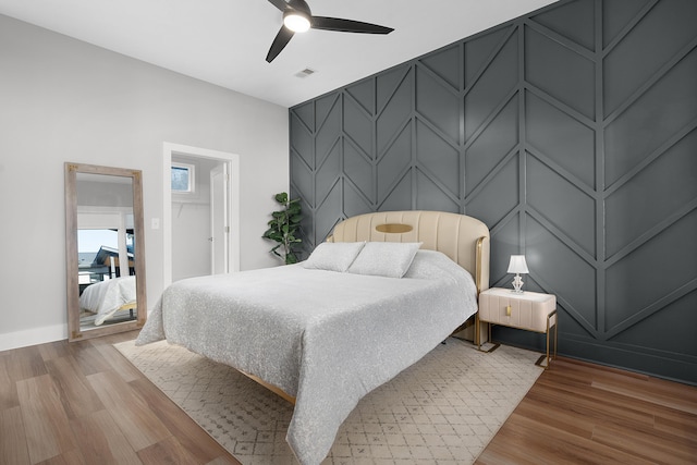 bedroom with ceiling fan, a decorative wall, an accent wall, visible vents, and light wood-style floors
