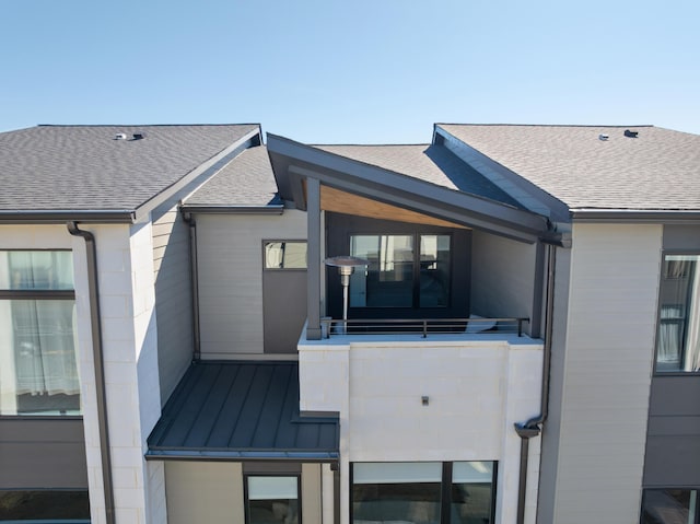 back of house with a standing seam roof, roof with shingles, and metal roof