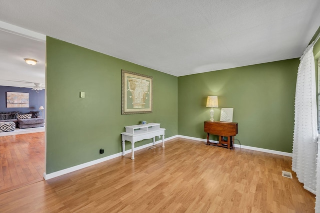 living area featuring light wood-style flooring, a textured ceiling, baseboards, and a ceiling fan