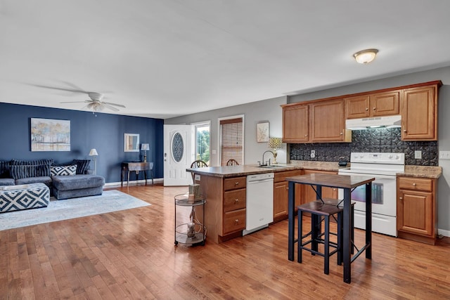 kitchen with a peninsula, white appliances, light wood-type flooring, and under cabinet range hood