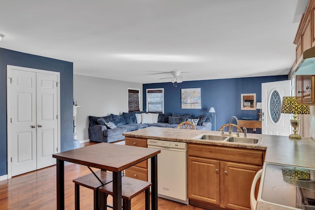 kitchen featuring a peninsula, range with electric cooktop, a sink, dishwasher, and light wood finished floors