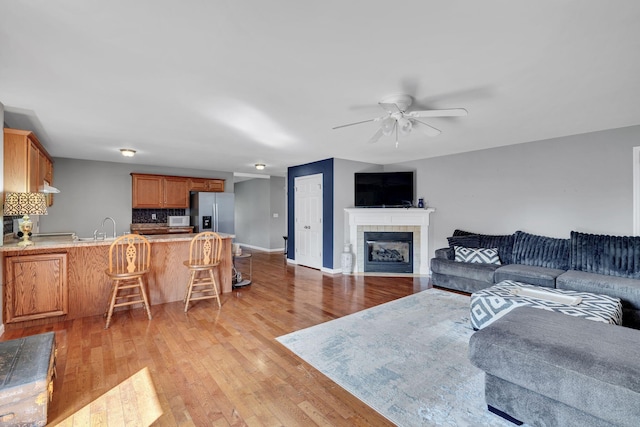 living room with light wood-style floors, ceiling fan, baseboards, and a tiled fireplace