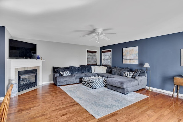 living area with light wood finished floors, a tiled fireplace, a ceiling fan, and baseboards