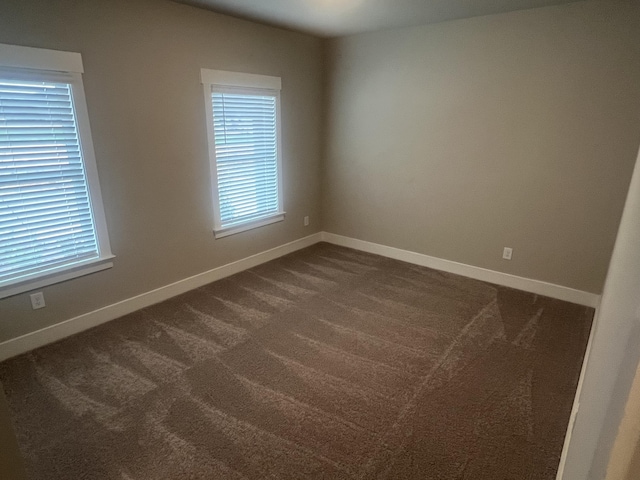 empty room featuring dark colored carpet, a healthy amount of sunlight, and baseboards