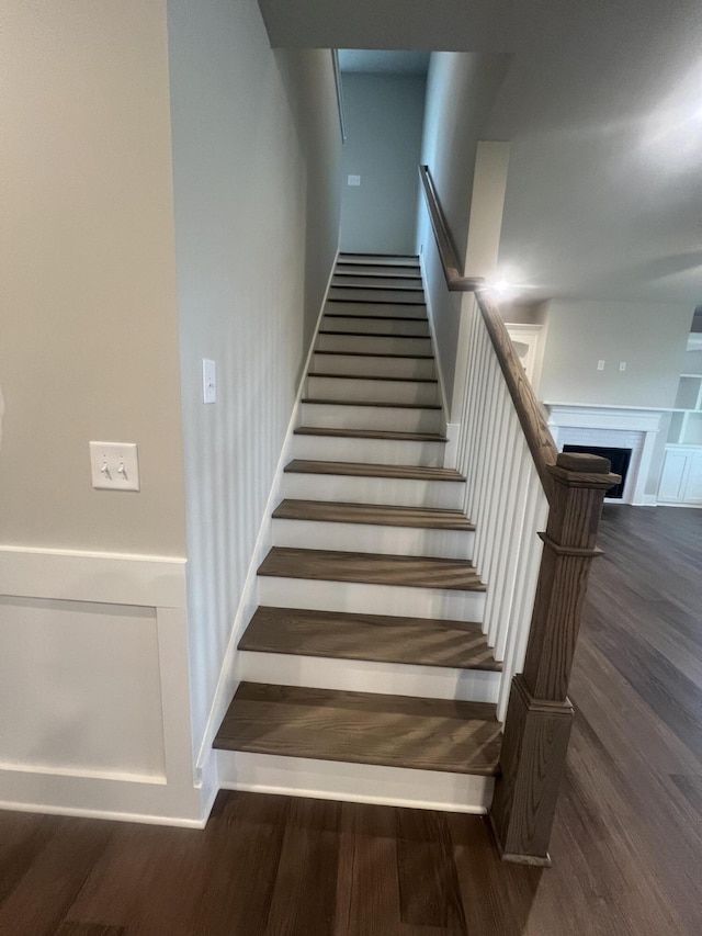 stairs featuring a wainscoted wall, a fireplace, and wood finished floors