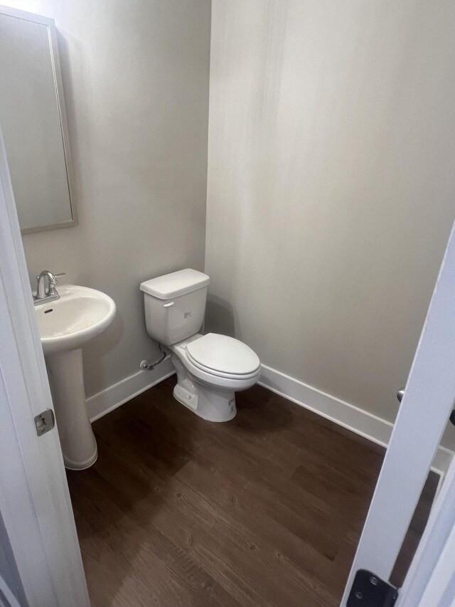 half bath with a sink, wood finished floors, toilet, and baseboards