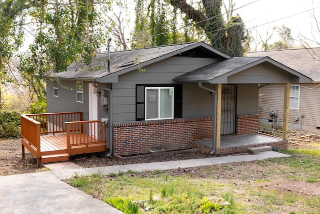 view of front facade featuring brick siding, a deck, and roof with shingles