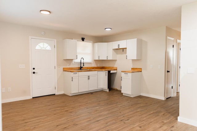 kitchen with butcher block counters, a sink, baseboards, white cabinets, and light wood-type flooring