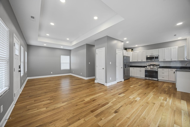 kitchen with visible vents, dark countertops, open floor plan, stainless steel appliances, and a raised ceiling