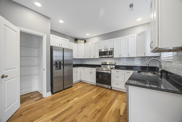 kitchen with dark stone countertops, visible vents, a sink, light wood-style floors, and appliances with stainless steel finishes