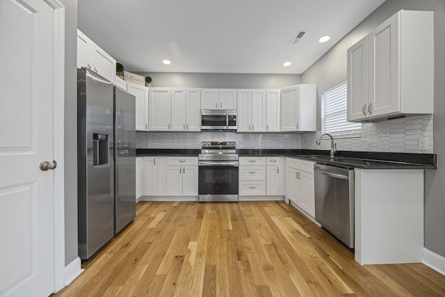 kitchen featuring light wood-type flooring, visible vents, a sink, backsplash, and stainless steel appliances