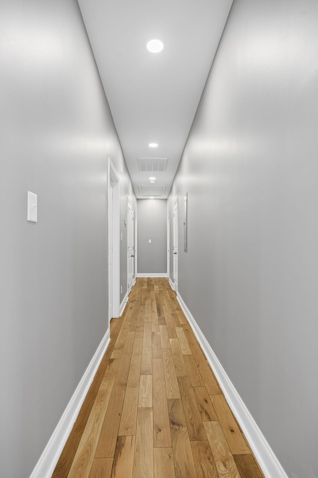 hallway with attic access, light wood-style floors, baseboards, and visible vents