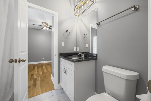 half bath with vanity, baseboards, ceiling fan, toilet, and marble finish floor