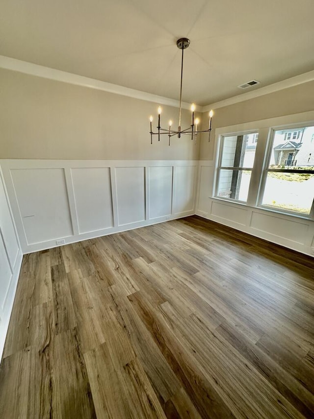 unfurnished dining area featuring visible vents, an inviting chandelier, wood finished floors, and a decorative wall