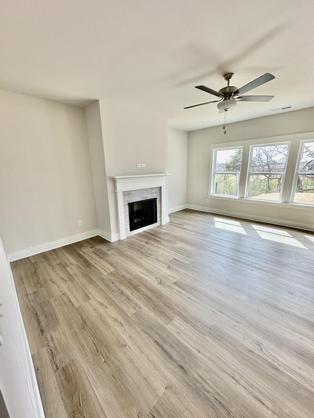 unfurnished living room with visible vents, baseboards, a fireplace, light wood-style floors, and a ceiling fan