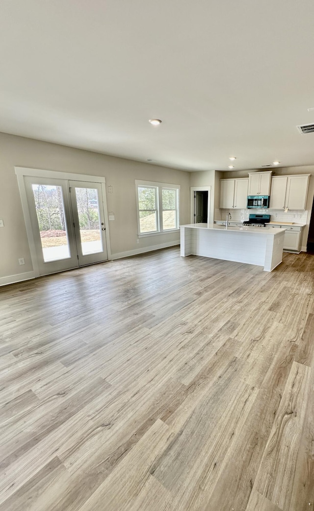 unfurnished living room featuring visible vents, light wood-style flooring, a sink, recessed lighting, and baseboards