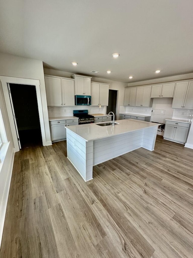 kitchen with a sink, light wood-type flooring, backsplash, and appliances with stainless steel finishes