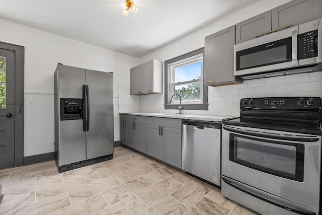 kitchen featuring light countertops, backsplash, gray cabinetry, appliances with stainless steel finishes, and a sink